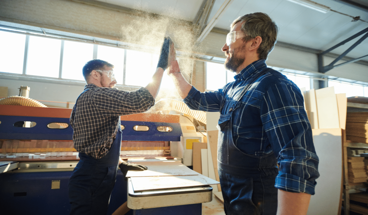two workers in a woodworking shop giving each other High Fives, and releasing potentially combustible dust into the air.