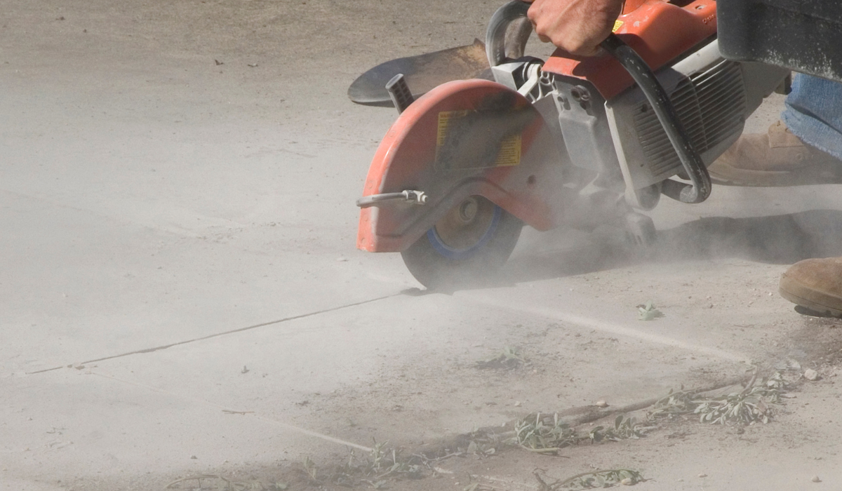 A masonry saw cutting into cement on the ground, during which time silica dust protection is critical
