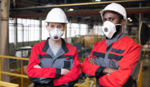 Two employees in red safety vests wearing hardhats and respirators, as part of their workplace respiratory protection program.